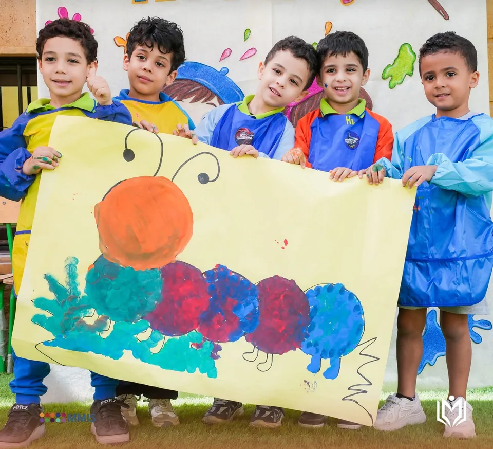 خمسة أطفال بمرايل الرسم يحملون لوحة دودة ملوّنة