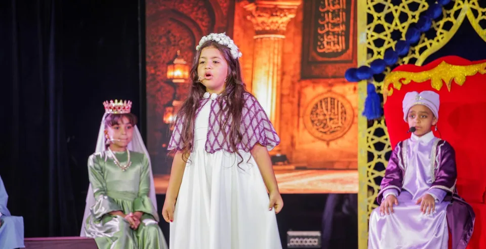 طالبة بفستان أبيض تتحدث على المسرح بجوار زملائها بالأزياء